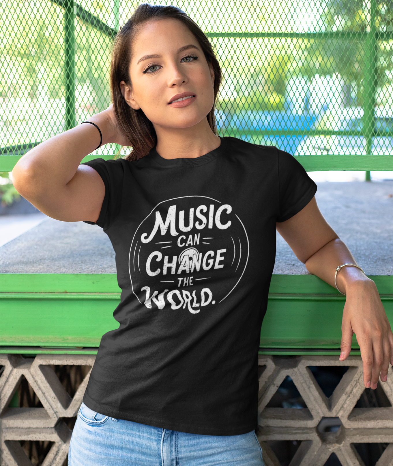 Woman wearing a black t-shirt with 'Music Can Change the World' text, standing against a green metal fence.