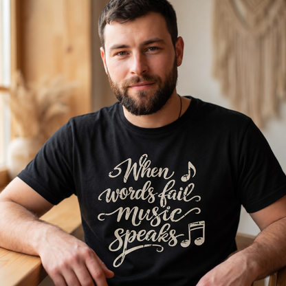 A man wearing a black t-shirt with the phrase 'When words fail music speaks' printed in a white cursive font with musical notes, set against a warm, softly blurred indoor background.